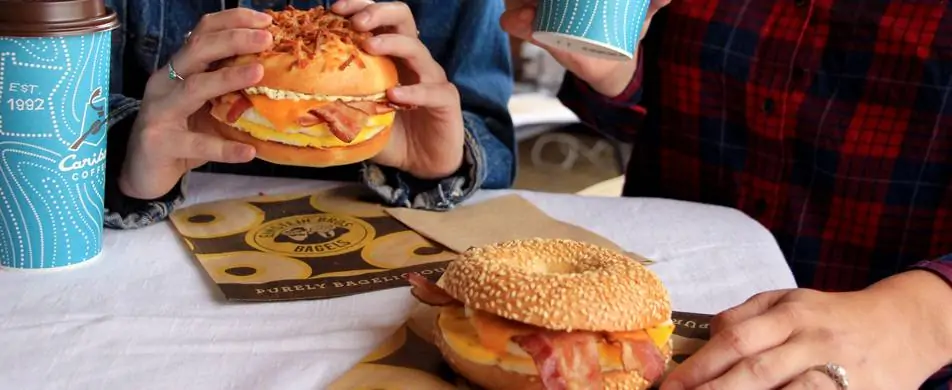 Couple eating Einstein Bros. bagel egg sandwiches with coffee